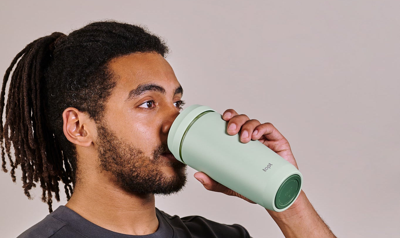 Man drinking from a green water bottle against a plain background
